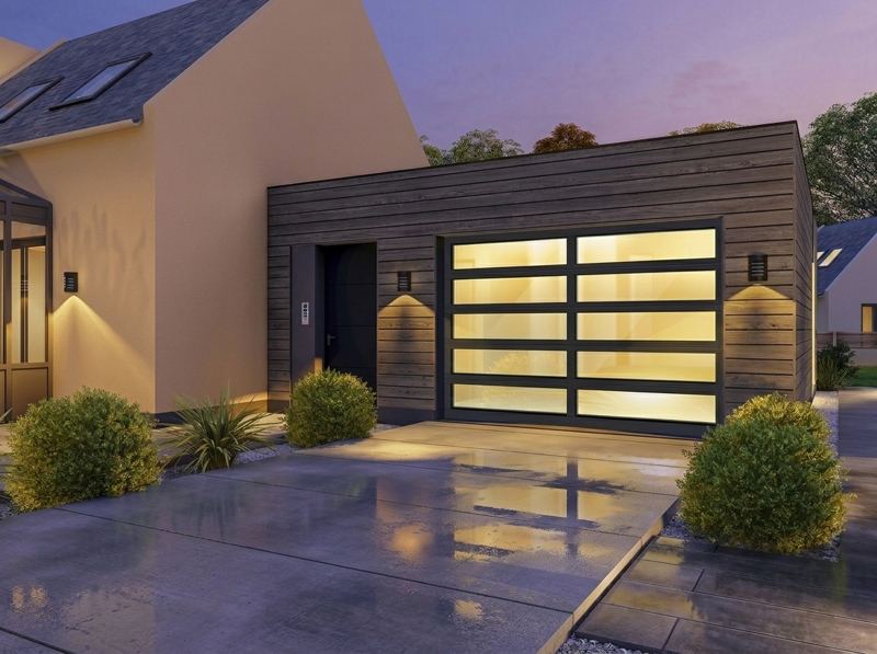 Crystal Series glass garage door with a slim black frame on a wood-clad garage at night