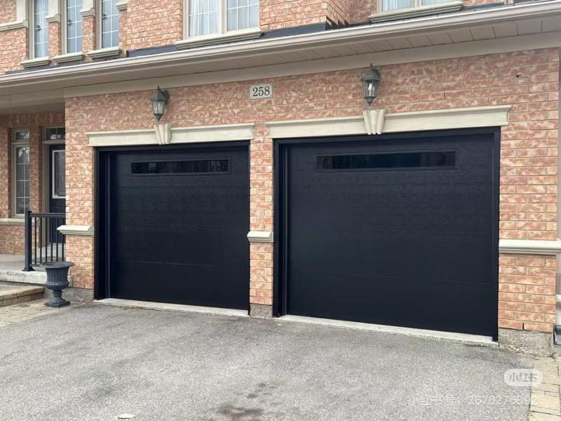 Two black modern garage doors with windows on a brick home