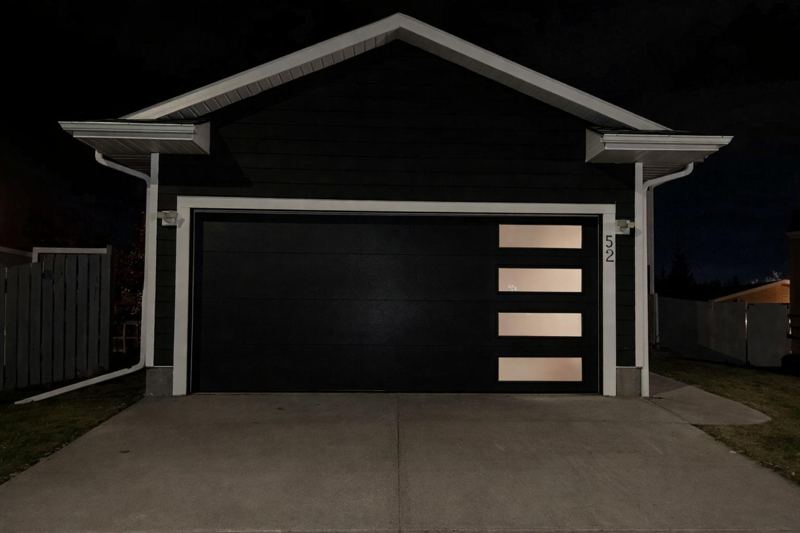 Black modern garage door with frosted side windows, at night