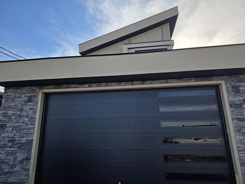 Black flush garage door with glass windows in a stone facade