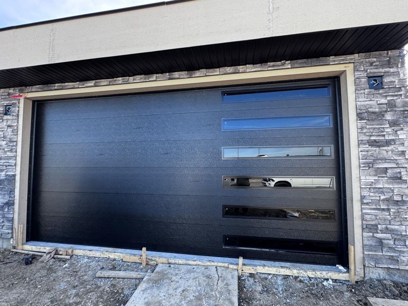 Black flush garage door with side windows in a stone facade