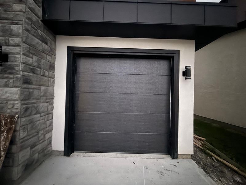 Black single garage door on a modern stone and stucco home